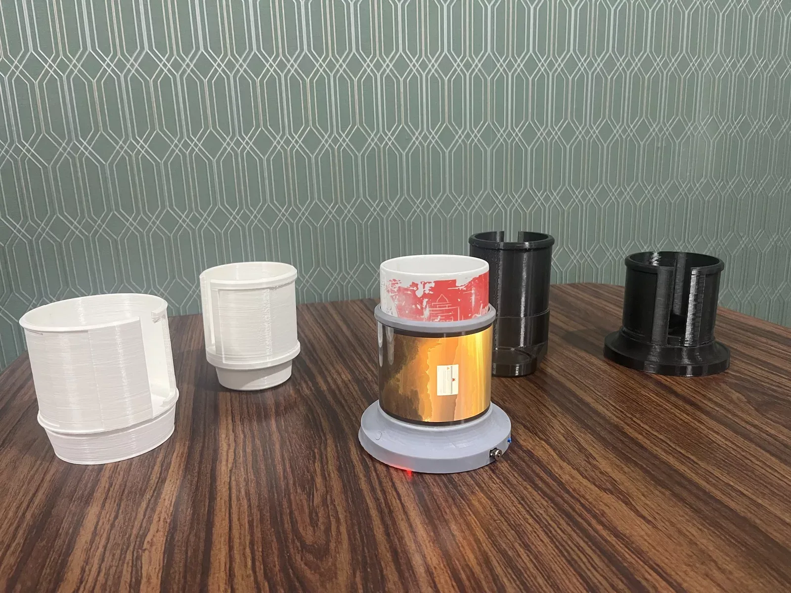 Successive 3D-printed enclosure iterations for the mug holder, ending in the final assembled unit