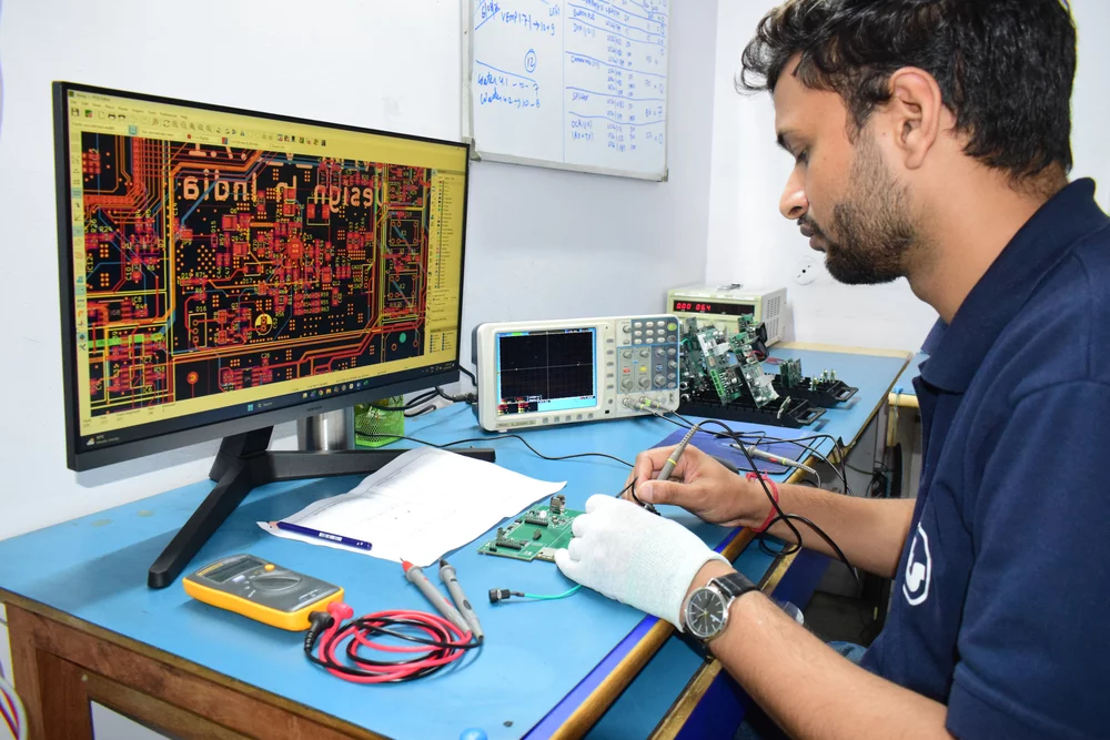 Engineer bench-testing a board against its PCB layout and an oscilloscope