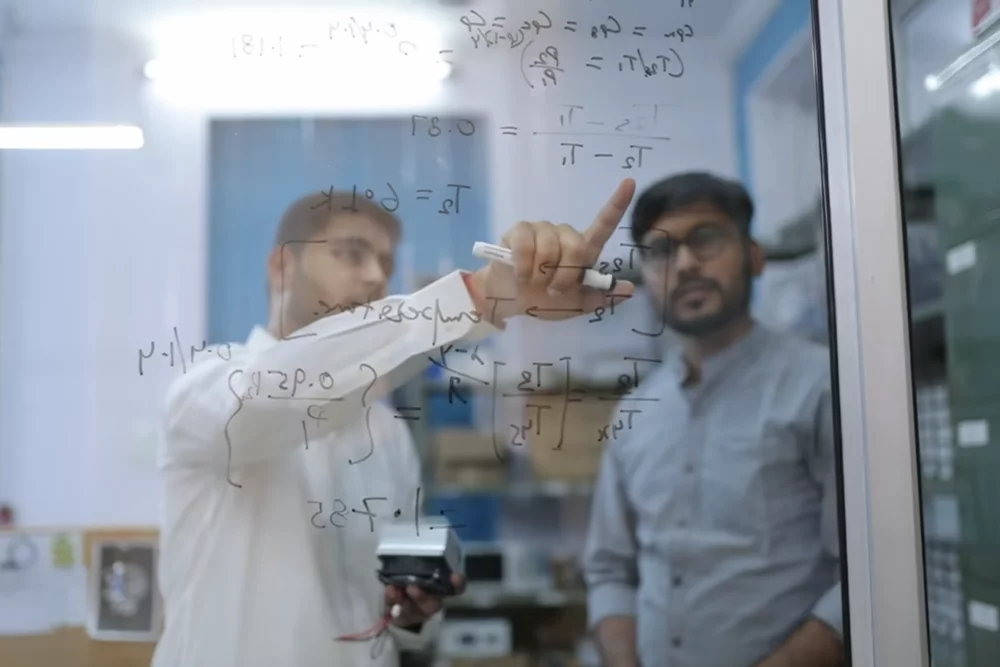 Two engineers working through thermal equations on a glass board